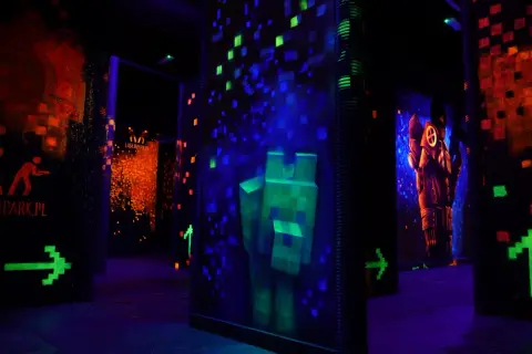 Mroczna arena do laser tag z neonowymi grafikami, strzałkami i postaciami.