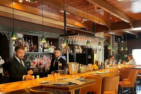 Banqueros sirviendo en uno de los restaurantes el ejido, con un ambiente acogedor y una barra de madera pulida.