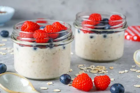 Zwei Gläser mit Overnight Oats, garniert mit Himbeeren und Blaubeeren. Perfekt für gesunde Overnight Oats Rezepte.