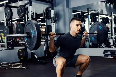 Un homme fait un squat avec une barre chargée, un exercice clé pour un programme musculation prise de masse.