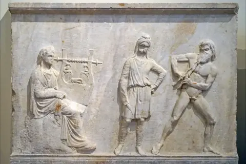 Bas-relief antique : une femme joue de la lyre, un homme au centre, et un homme nu jouant de la cithare, symbole Apollon.