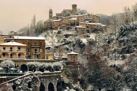 Borgo innevato in Toscana. Case antiche e alberi coperti di neve creano un paesaggio fiabesco, dimostrando che sì, a volte fa neve in Toscana.