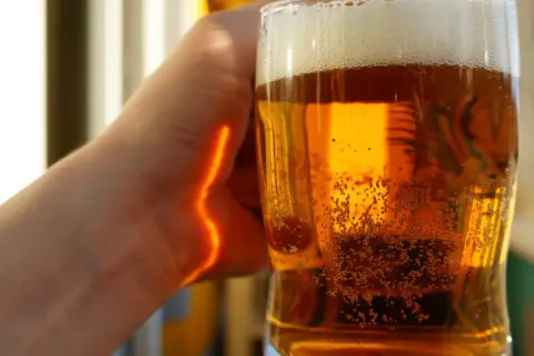 Ręka trzymająca szklankę złocistego piwa z pianką. Czy piwo jest zdrowe? Pytanie pozostaje otwarte, gdy bąbelki tańczą w szkle.