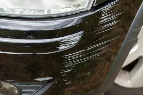 Porysowany czarny zderzak, potencjalne przyczyny trzeszczenia zderzaka podczas jazdy po nierównościach.