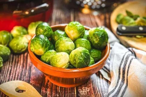 Frischer Rosenkohl in einer Schale, bereit für leckere Rosenkohl Rezepte. Ein Holzlöffel und ein Küchentuch liegen daneben.