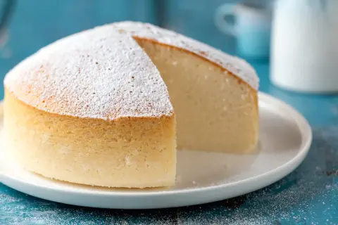 Una soffice torta nuvola, cosparsa di zucchero a velo, attende di essere gustata su un piatto bianco.