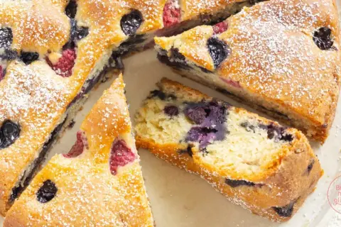 Saftiger, veganer Kuchen mit Blaubeeren und Himbeeren, bestäubt mit Puderzucker. Ein Genuss für alle!