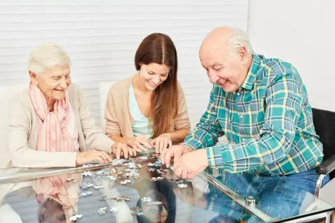Trois personnes, deux aînées et une jeune femme, s'amusent à assembler un puzzle, une activité stimulante pour les jeux de mémoire.