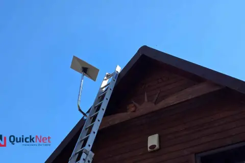 Antena satelitarna Starlink zamontowana na dachu drewnianego domu. Obok drabina, gotowa do pracy.