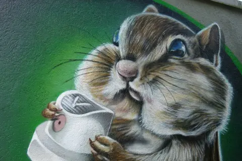 Graffiti eines Eichhörnchens, das eine Spraydose hält, vor grünem Hintergrund.