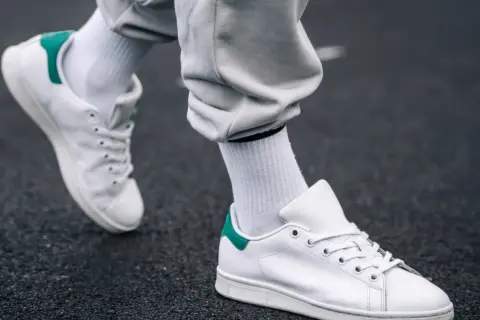 Białe sneakersy z zielonym akcentem na pięcie, na ciemnym tle. Dowiedz się, jak pozbyć się zagięć na butach, by wyglądały jak nowe.