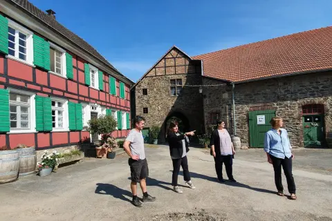 Vier Personen stehen vor einem historischen Fachwerkhaus und einem steinernen Torbogen auf dem Gut Nesselrath.