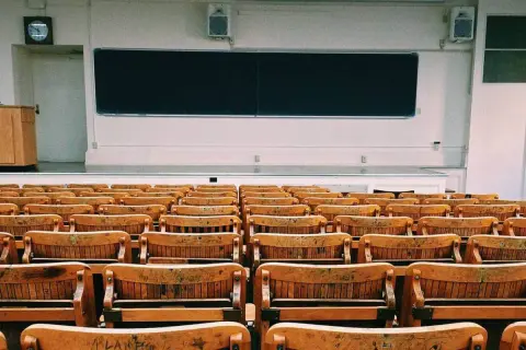 Aula vacía con asientos de madera y pizarra. Un profesor podría hablar aquí, pero para explicar la diferencia entre speak y talk, necesitaría a los estudiantes.