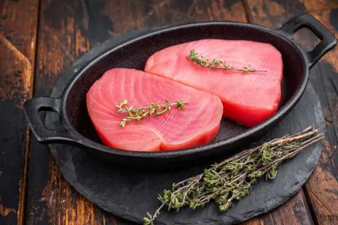 Deux beaux pavés de thon rouge cru, ornés de brins de thym frais, prêts pour une recette savoureuse.