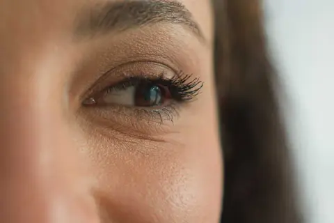Gros plan sur un œil marron, cils longs et recourbés. Une étape maquillage yeux réussie, le regard est intense.