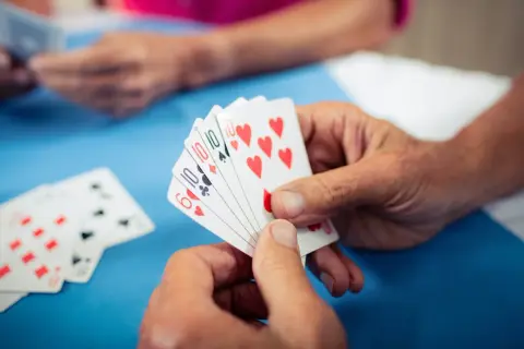 Hände halten Spielkarten, ein Spiel zur Förderung der kognitiven Fähigkeiten bei Demenz.