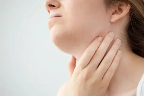 Mano che tocca il collo, forse per sentire i linfonodi sottomentali ingrossati.