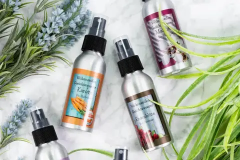 Vier Sprühflaschen mit Gesichtswasser, darunter Karotte und Rosenblüte. Ein Hydrolat ist ein destilliertes Pflanzenwasser, das bei der Herstellung ätherischer Öle anfällt.