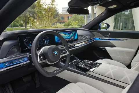 Wnętrze BMW 740d z nowoczesnym panelem cyfrowym, podświetlanymi detalami i komfortowymi, białymi fotelami.