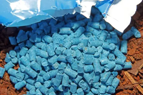 Ein blauer Haufen Schneckenkorn giftig liegt auf brauner Erde. Vorsicht, nicht für Kinder oder Haustiere!
