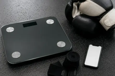 Boxing gloves, hand wraps, a scale, and a smartphone are laid out, ready for an amateur boxer to check their weight for the correct amatuer boxing weight classes.