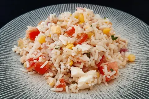 Une généreuse portion de salade de riz thon, garnie de dés de tomates, de maïs et d'œufs durs, sur une assiette texturée.