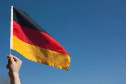 Ręka trzyma flagę Niemiec na tle błękitnego nieba. Chcesz wiedzieć, jak zaadresować list do Niemiec?