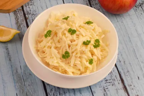 Pyszna surówka z selera i jabłka, udekorowana natką pietruszki, na drewnianym blacie.