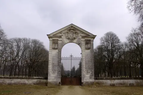 Portail monumental menant au **château de Richelieu**, avec une grille en fer forgé et des arbres dénudés en arrière-plan.