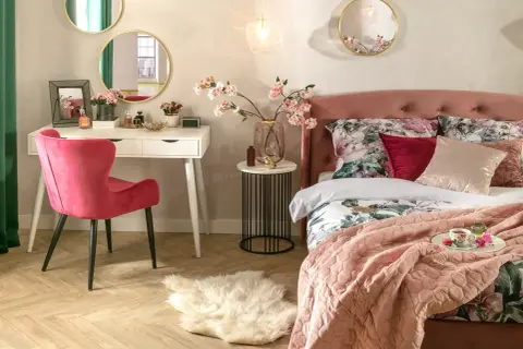 Elegancka toaletka w sypialni z różowym krzesłem, lustrami i kwitnącymi gałązkami wiśni.