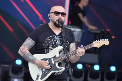 Łysy gitarzysta z tatuażami gra na białej gitarze. W tle klawiszowiec. Koncert, jakby to były kombi piosenki alfabetycznie.