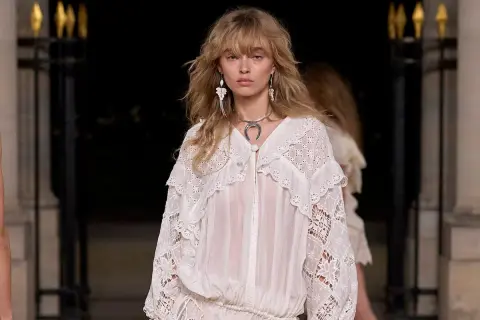 Modelo luce un vestido blanco con encaje, estilo boho, con pendientes largos y collar plateado.