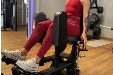 Femme en tenue de sport rouge travaillant son abducteur muscle sur une machine de musculation.