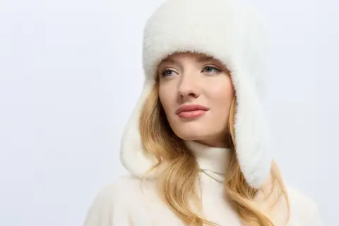 Blondynka w białej, futrzanej czapce uszatce, prezentującej najmodniejsze nakrycia głowy.