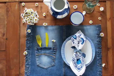 Tovagliette americane fai da te in denim con tasca porta posate, decorate con margherite e un servizio da tavola blu e bianco.