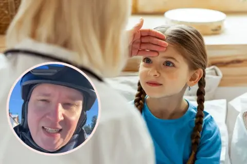 Lekarz bada gorączkującą dziewczynkę, sprawdzając jej czoło. W tle widać mężczyznę w kasku. Objawy adenowirusa mogą być różne.