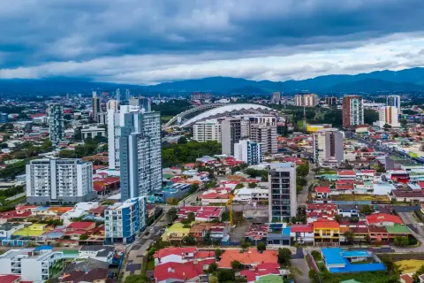 Vy över San José, Costa Rica, med moderna skyskrapor och färgglada hus under en molnig himmel.