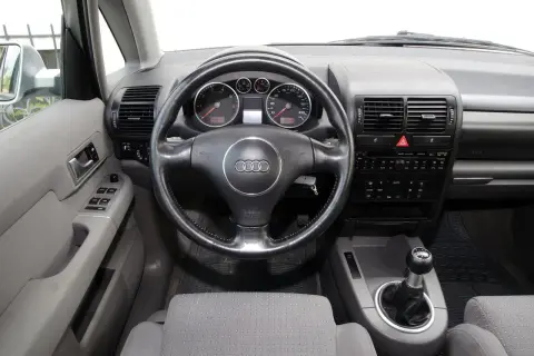 Wnętrze Audi A2 z kierownicą, deską rozdzielczą i dźwignią zmiany biegów. Widoczne wskaźniki, radio i przyciski.