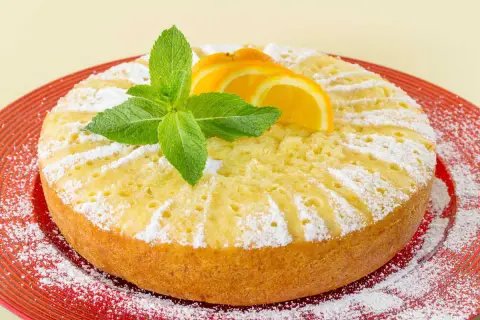 Torta soffice all'arancia, ricetta della nonna, decorata con fettine d'arancia e menta fresca, cosparsa di zucchero a velo.