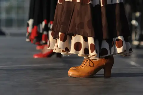 Taconeo flamenco: un zapato de cuero marrón con cordones y tacón, parte de un vestido de lunares, listo para bailar.