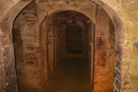 Corridoio sotterraneo con archi in mattoni e pietra a Monsampolo del Tronto, evocando misteri antichi.