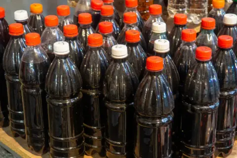 Butelki z ciemnym płynem, być może domowym winem cannonau, stoją obok siebie na półce.
