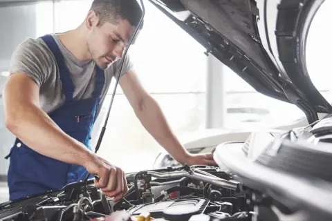 Mechanik w niebieskim kombinezonie pracuje przy silniku. Zastanawiasz się, czy warto płacić za przedłużoną gwarancję w warsztacie sieciowym zamiast u pana Mirka?