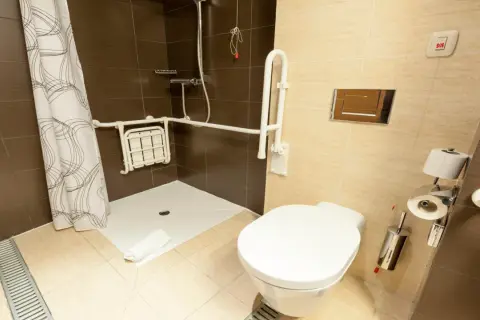 Salle de bain adaptée avec douche PMR, siège rabattable, barres d'appui et bouton d'urgence.
