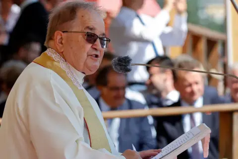 Ojciec Tadeusz Rydzyk przemawia do mikrofonu. W tle widać ludzi, a także fragmenty budowli. W czasach rządu PiS, fundacje związane z ojcem Rydzykiem otrzymywały znaczące dotacje.
