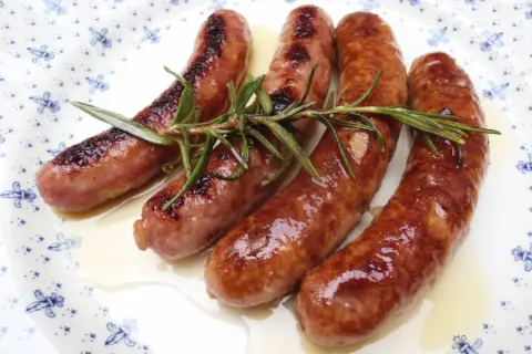 Salchichas doradas en salsa, con romero fresco, servidas en un plato blanco con diseño azul.