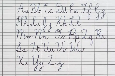The alphabet in cursive, from A to Z, is written in neat blue ink on lined paper. The handwriting is perfect in cursive, showing each letter's formation.