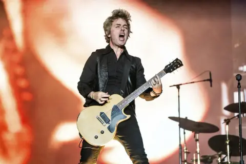 Billie Joe Armstrong z Green Day Saviors śpiewa i gra na gitarze na scenie, z perkusją w tle.