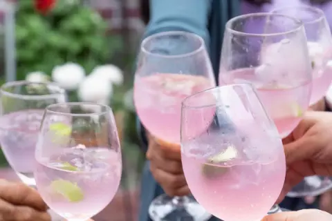 Fünf Gläser mit pinkfarbenem Sarti Spritz, garniert mit Limette, stoßen an.