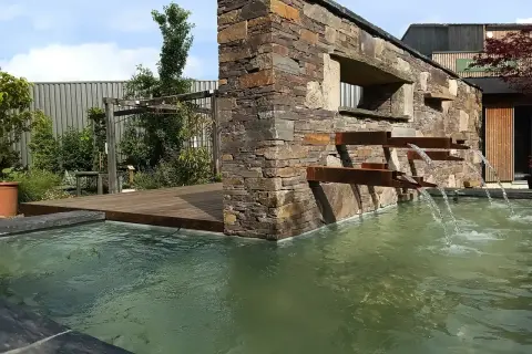 La mare aux plantes, avec sa cascade moderne en pierre et métal, invite à la détente. L'eau ruisselle doucement dans le bassin verdoyant.